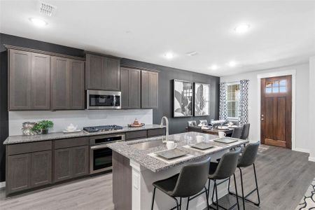 Kitchen featuring stainless steel appliances, sink, light stone countertops, a breakfast bar, and light hardwood / wood-style floors