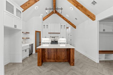 Kitchen with beam ceiling, a center island, stainless steel appliances, and white cabinets