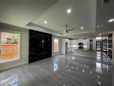 Unfurnished living room with ceiling fan, a raised ceiling, and light tile floors