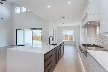 Kitchen with tasteful backsplash, sink, white cabinetry, light hardwood / wood-style floors, and pendant lighting