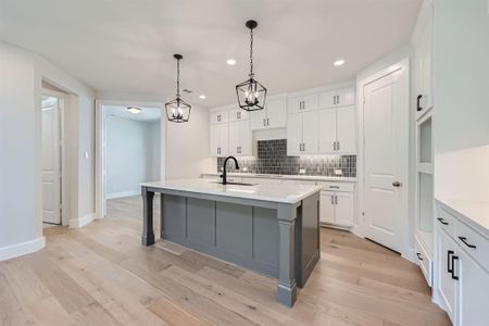 Kitchen featuring light hardwood / wood-style flooring, hanging light fixtures, decorative backsplash, a kitchen island with sink, and white cabinetry