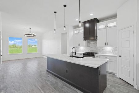 Kitchen with an island with sink, custom range hood, white cabinets, gas stove, and sink