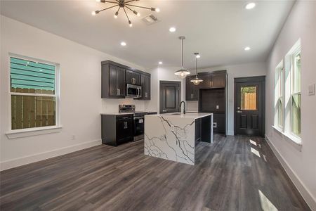 Kitchen with dark wood-type flooring, a center island with sink, electric range oven, and hanging light fixtures