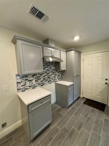 Kitchen with gray cabinets, tasteful backsplash, and range hood