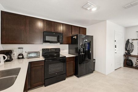 Kitchen with dark brown cabinetry, black appliances, sink, and light tile patterned floors