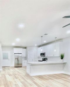 Kitchen with appliances with stainless steel finishes, white cabinets, ceiling fan, and decorative light fixtures