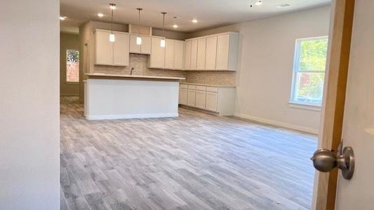 Kitchen with light wood-type flooring, white cabinetry, decorative backsplash, and hanging light fixtures