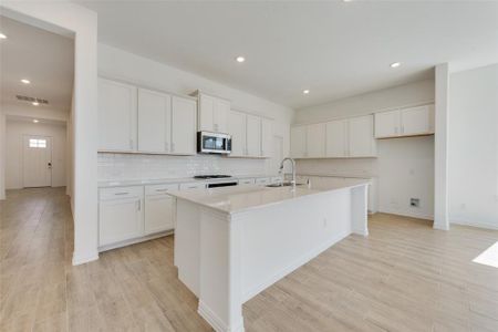 Kitchen with light hardwood / wood-style floors, white cabinetry, a center island with sink, sink, and tasteful backsplash