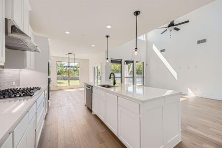 Kitchen with white cabinetry, ventilation hood, ceiling fan, a center island with sink, and sink