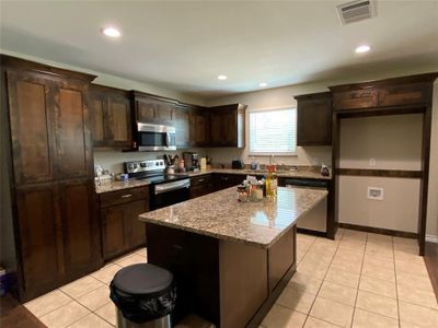 Kitchen featuring light stone countertops, dark brown cabinets, a kitchen island, light tile floors, and appliances with stainless steel finishes