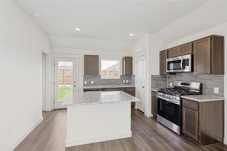 Kitchen with lofted ceiling, hardwood / wood-style floors, backsplash, a kitchen island, and stainless steel appliances