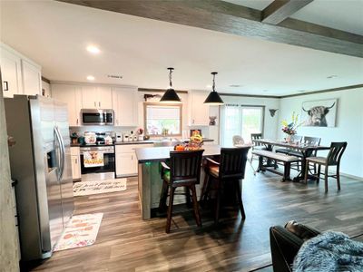 Kitchen featuring a kitchen island, dark wood-type flooring, pendant lighting, white cabinetry, and appliances with stainless steel finishes