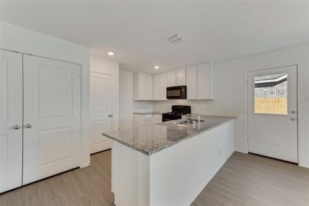 Kitchen featuring light stone countertops, white cabinets, black appliances, and kitchen peninsula