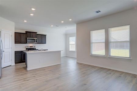 Kitchen with stainless steel appliances, dark brown cabinets, light hardwood / wood-style flooring, a center island with sink, and sink