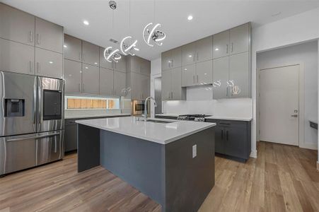 Kitchen featuring an island with sink, hanging light fixtures, stainless steel fridge with ice dispenser, gray cabinets, and light hardwood / wood-style floors