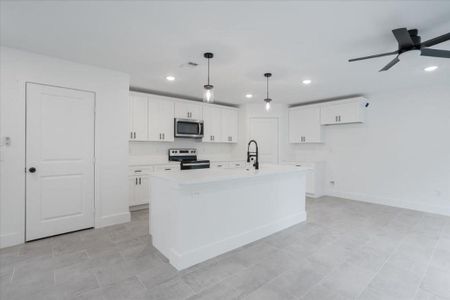 Kitchen featuring white cabinets, appliances with stainless steel finishes, a kitchen island with sink, and ceiling fan