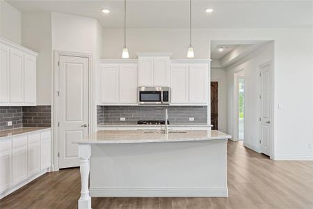 Kitchen featuring light wood-type flooring, backsplash, light stone counters, and white cabinets