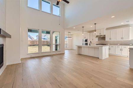 Kitchen with stainless steel microwave, a center island with sink, decorative light fixtures, light wood-type flooring, and white cabinetry