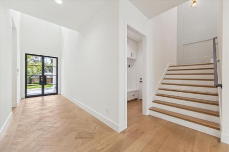 Adjacent to the foyer, the mudroom offers convenient access to the attached garage. It features engineered white oak flooring, a built-in bench with drawers underneath, and sculptural clothing hooks against Pennygap wall detailing. Recessed LED lighting illuminates the space, enhancing its functionality and style.