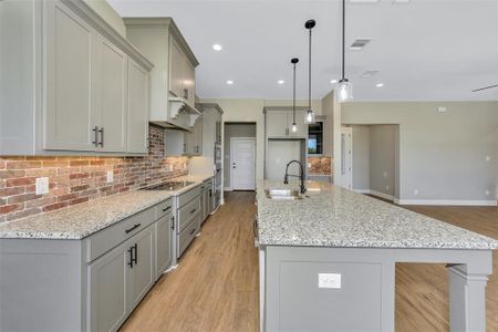 Kitchen featuring light wood-type flooring, backsplash, gray cabinetry, and hanging light fixtures