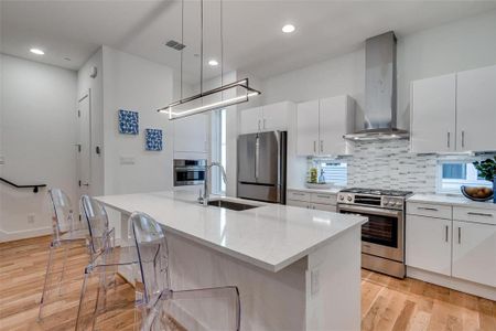 Kitchen featuring pendant lighting, a kitchen island with sink, sink, wall chimney exhaust hood, and appliances with stainless steel finishes