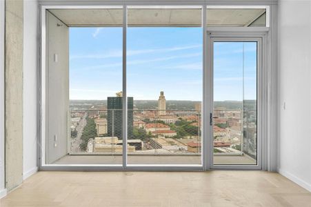 An open floor plan and floor-to-ceiling glass panels offering stunning city views, including the UT Campus building. Modern furnishings and neutral tones create a stylish and inviting space perfect for relaxation and enjoying the urban scenery.