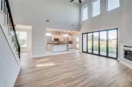 Unfurnished living room featuring light wood-type flooring, a high ceiling, ceiling fan, and sink