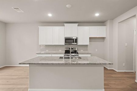 This light and bright kitchen features a large quartz island, white cabinets, a large sink overlooking your family room, recessed lighting, and beautiful backsplash.