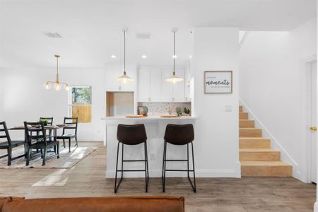 Kitchen with white cabinets, decorative light fixtures, tasteful backsplash, and light hardwood / wood-style flooring