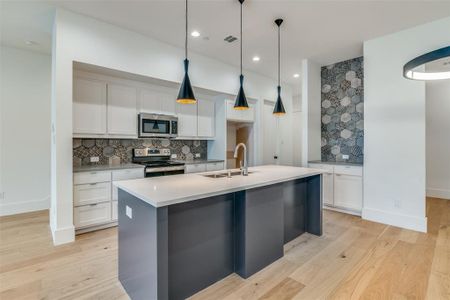 Kitchen featuring light hardwood / wood-style floors, stainless steel appliances, a center island with sink, backsplash, and sink