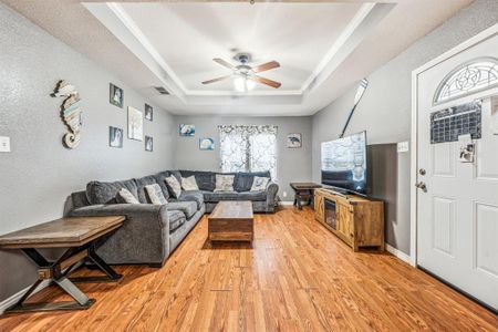 Living room featuring a tray ceiling, ceiling fan, and light hardwood / wood-style flooring