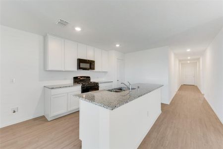 Kitchen with light hardwood / wood-style flooring, white cabinets, black appliances, and an island with sink