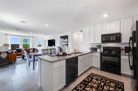Kitchen with white cabinetry, black appliances, sink, light stone counters, and kitchen peninsula