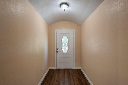 Doorway featuring dark wood-type flooring, vaulted ceiling, and a textured ceiling
