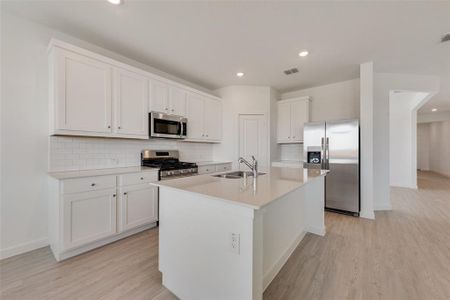 Kitchen with white cabinets, an island with sink, light wood-type flooring, sink, and stainless steel appliances