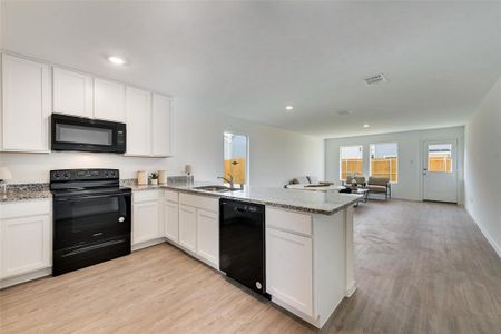 Kitchen featuring sink, kitchen peninsula, white cabinetry, black appliances, and light wood-type flooring