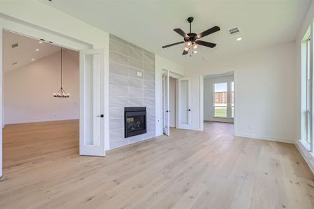 Unfurnished living room with a tiled fireplace, light hardwood / wood-style flooring, lofted ceiling, tile walls, and ceiling fan