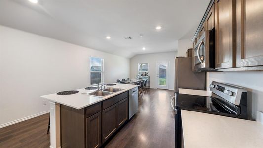 Kitchen with dark hardwood / wood-style flooring, appliances with stainless steel finishes, a kitchen island with sink, and sink