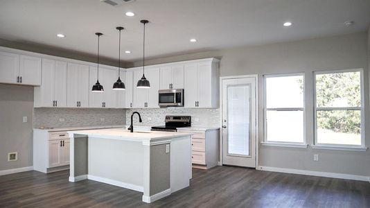 Kitchen featuring hanging light fixtures, stainless steel appliances, dark hardwood / wood-style floors, white cabinets, and a center island with sink