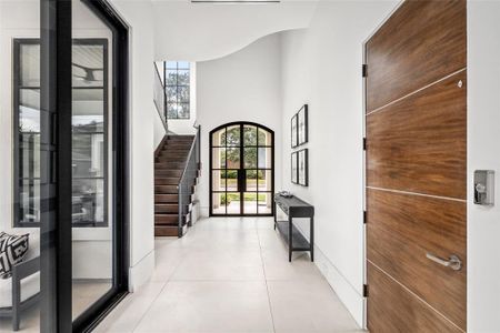 This stunning entryway features sleek stone floors and soaring high ceilings, offering an open and airy feel. The glass and steel double doors provide a striking entrance, allowing natural light to flood the space. The modern staircase creates the perfect blend of contemporary design and welcoming ambiance.