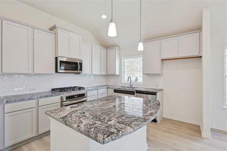 Kitchen featuring a center island, stainless steel appliances, light stone countertops, and vaulted ceiling