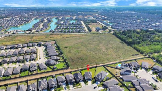 This aerial photo showcases a residential area with numerous homes situated along curved streets near bodies of water, with a large open field adjacent to the community, offering potential for expansion or natural views. A red marker indicates a specific property within this suburban landscape.