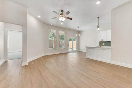 Unfurnished living room with ceiling fan with notable chandelier and light hardwood / wood-style flooring