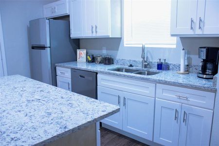 Kitchen with dark wood-type flooring, stainless steel appliances, sink, light stone countertops, and white cabinetry