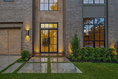 A sleek and inviting entryway features double glass doors framed by floor-to-ceiling windows, allowing natural light to flood into the open-concept layout. Thoughtful exterior lighting highlights the home’s architectural features.