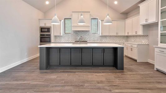 Kitchen with tasteful backsplash, oven, sink, black microwave, and a kitchen island with sink