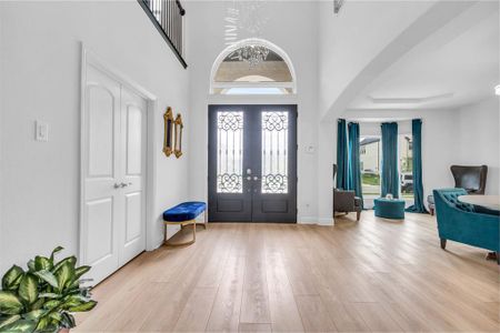 Entryway featuring a high ceiling, french doors, light hardwood / wood-style flooring, and a notable chandelier