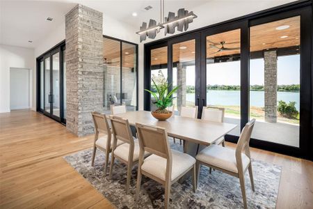 Dining room featuring a water view, plenty of natural light, light wood-type flooring, and decorative columns