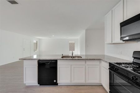 Kitchen with light wood-type flooring, sink, white cabinetry, and black appliances