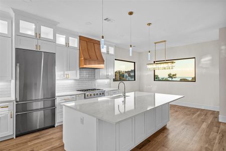 Kitchen featuring stainless steel appliances, a center island with sink, custom range hood, and white cabinetry